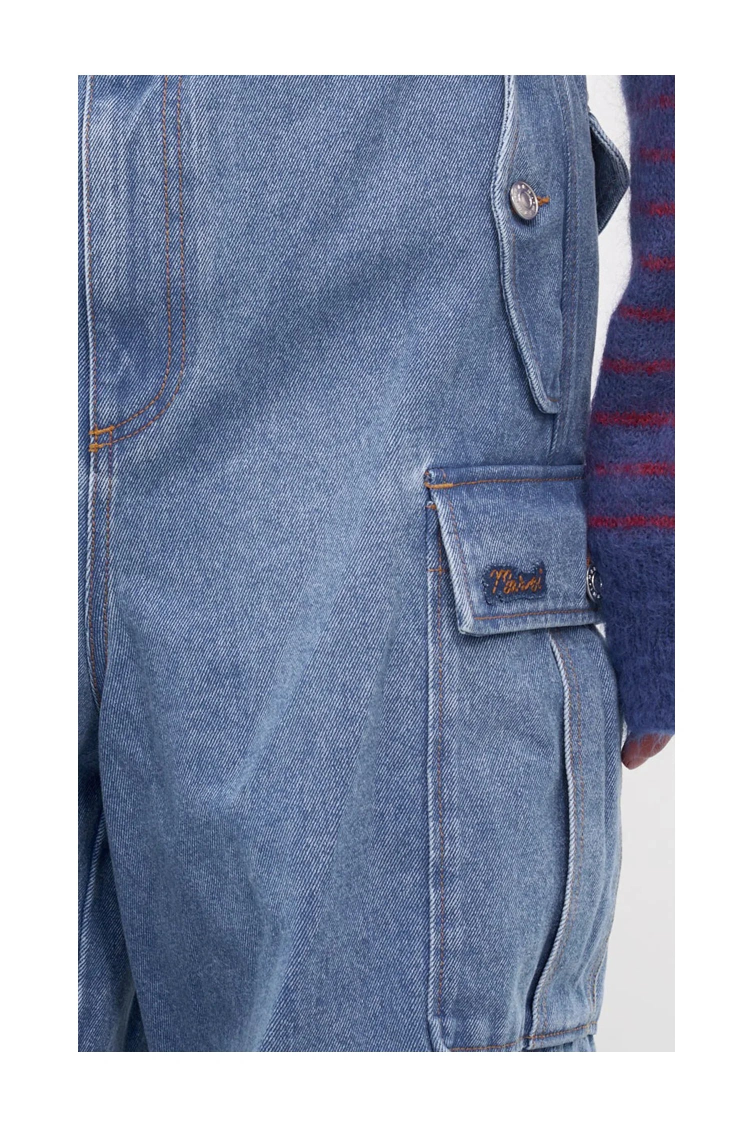 Close-up of blue denim cargo pants with flap pocket and visible stitching, worn with a striped sweater sleeve