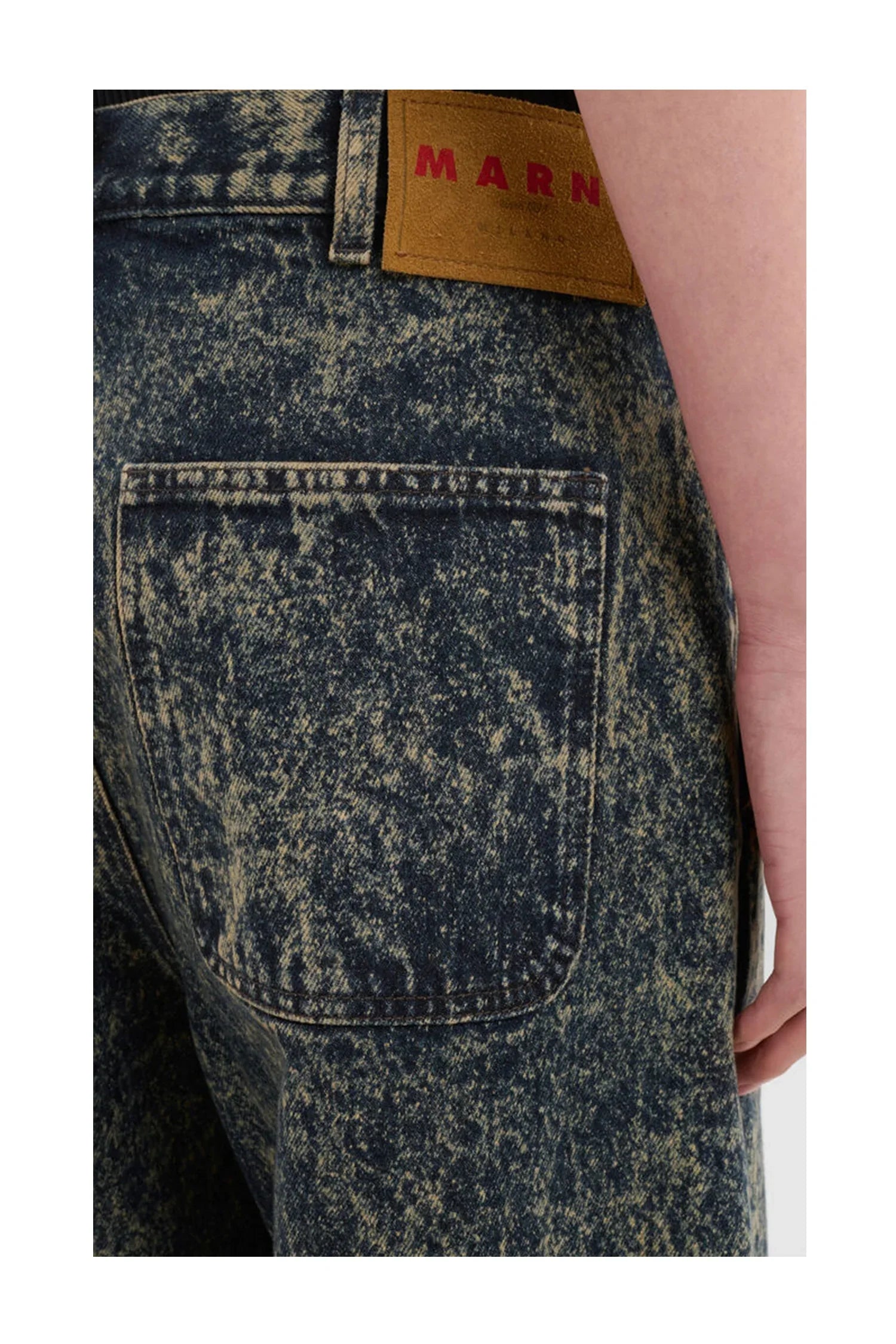 Close-up of acid-wash denim jeans back pocket with brown Marni brand label and visible arm