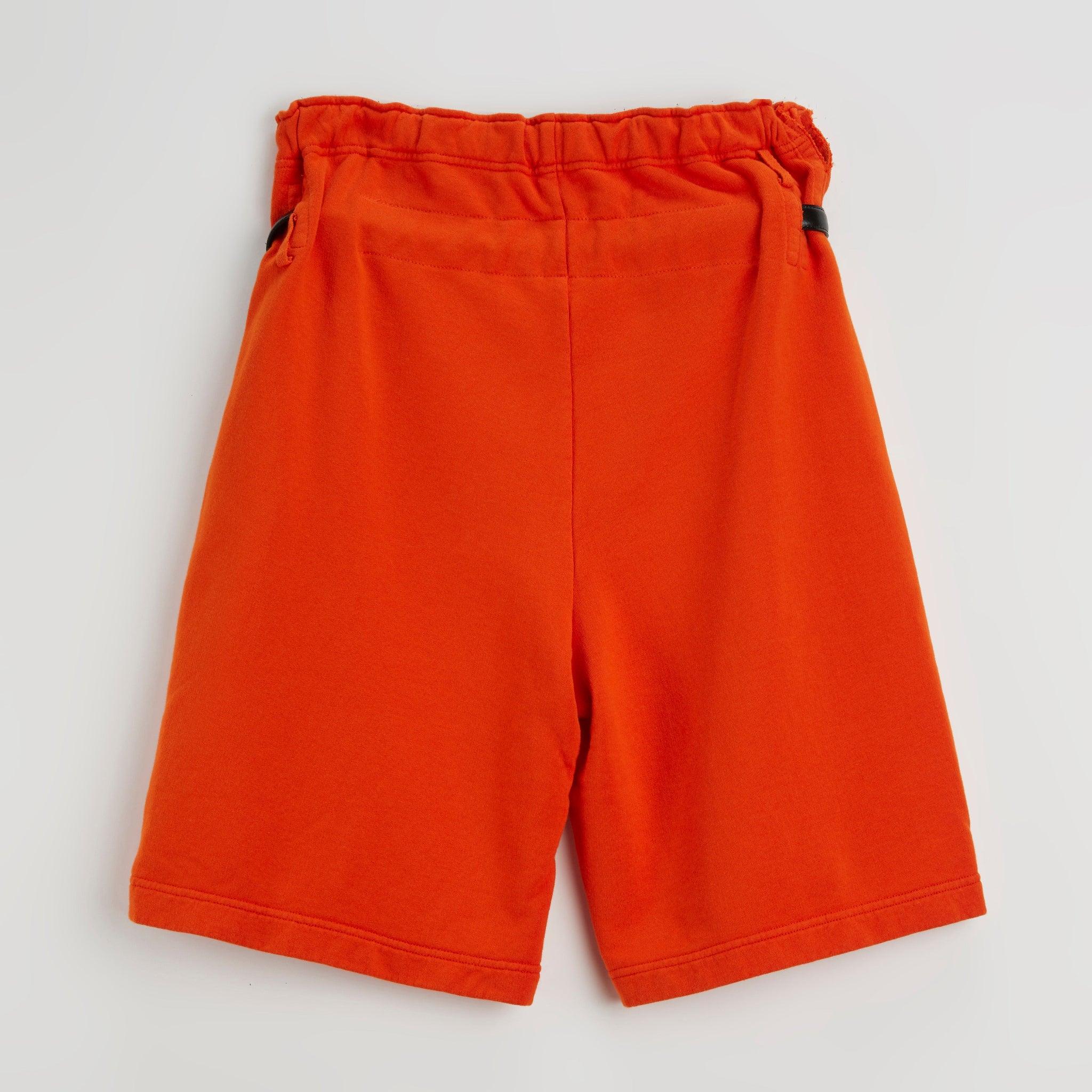 Back view of bright orange athletic shorts with elastic waistband and black buckle detail