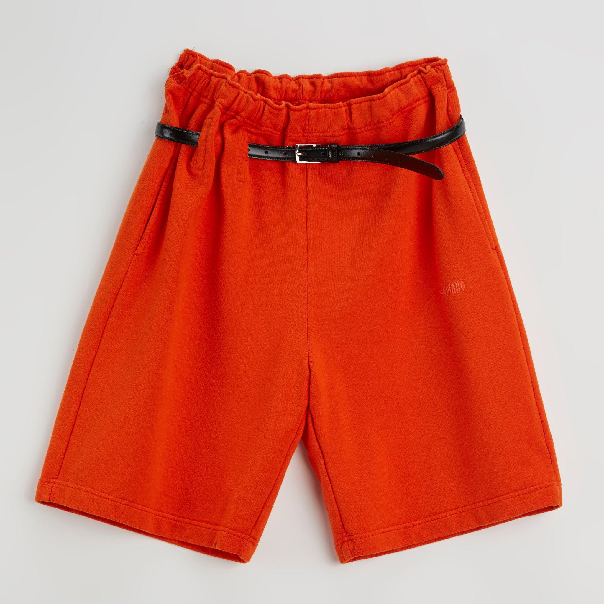 Bright orange athletic shorts with an elastic waistband and thin black belt on white background