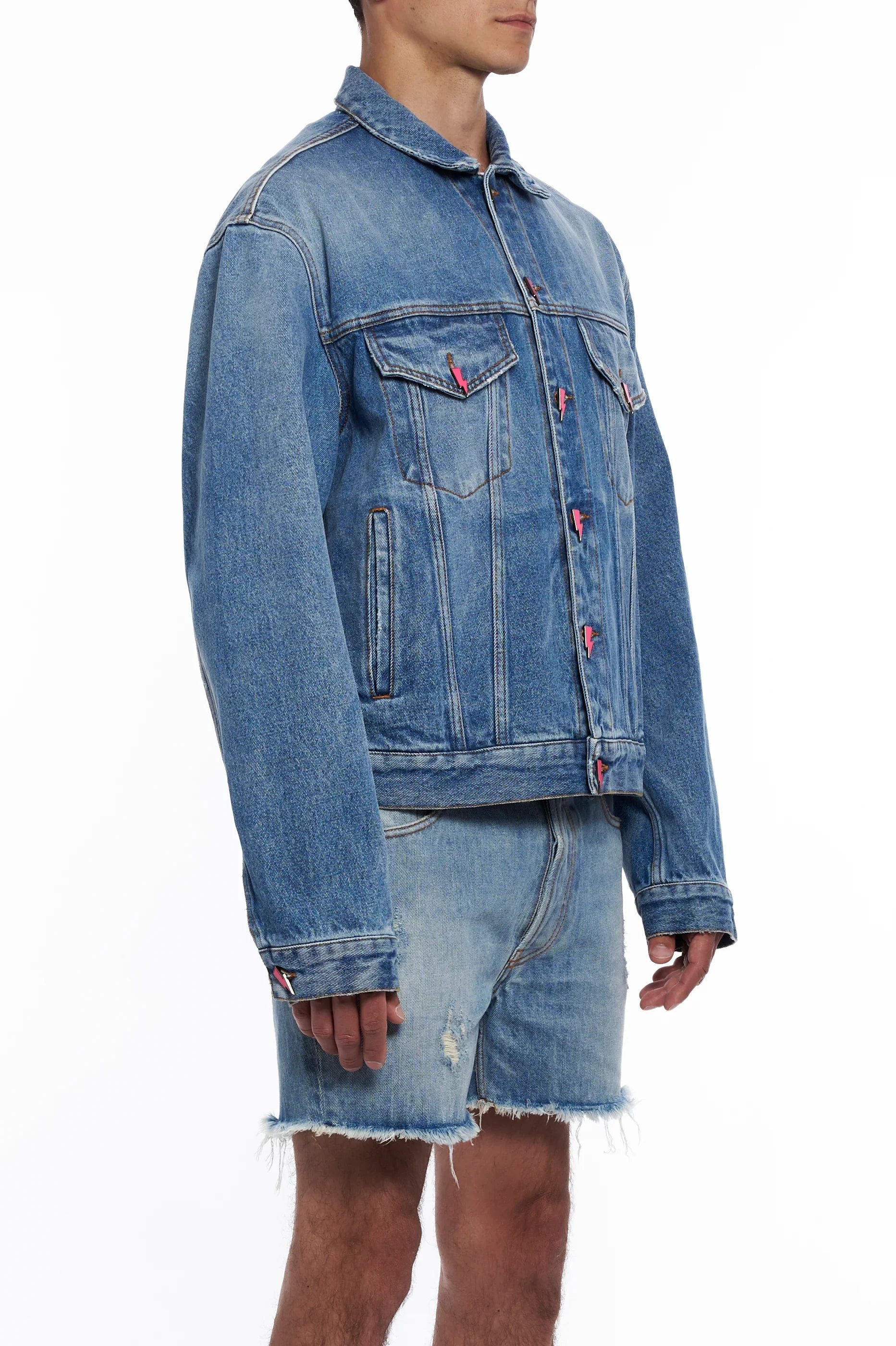 Man wearing light blue denim jacket with lightning bolt buttons and matching frayed denim shorts