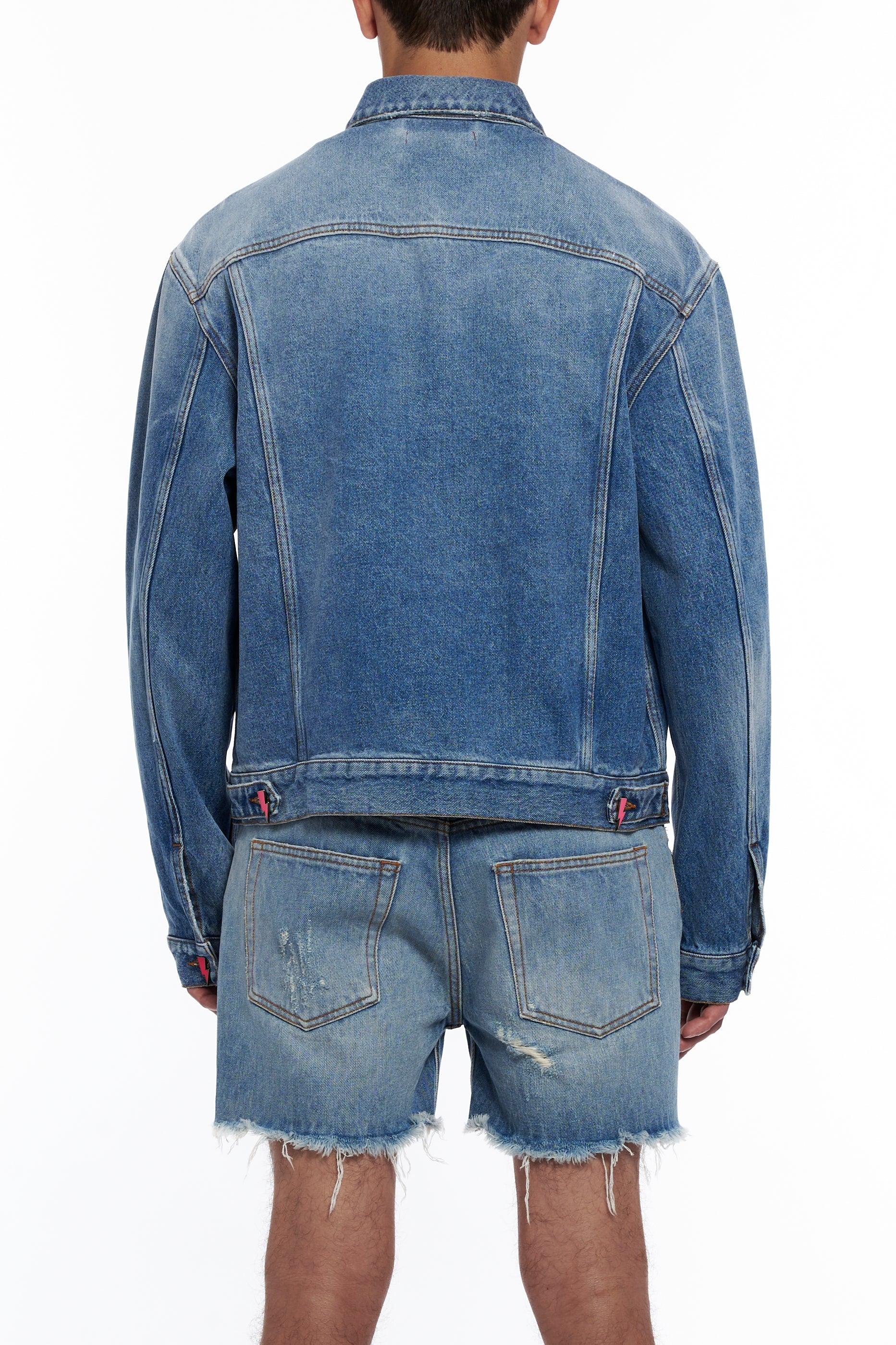 Back view of person wearing blue denim jacket and distressed denim shorts on white background