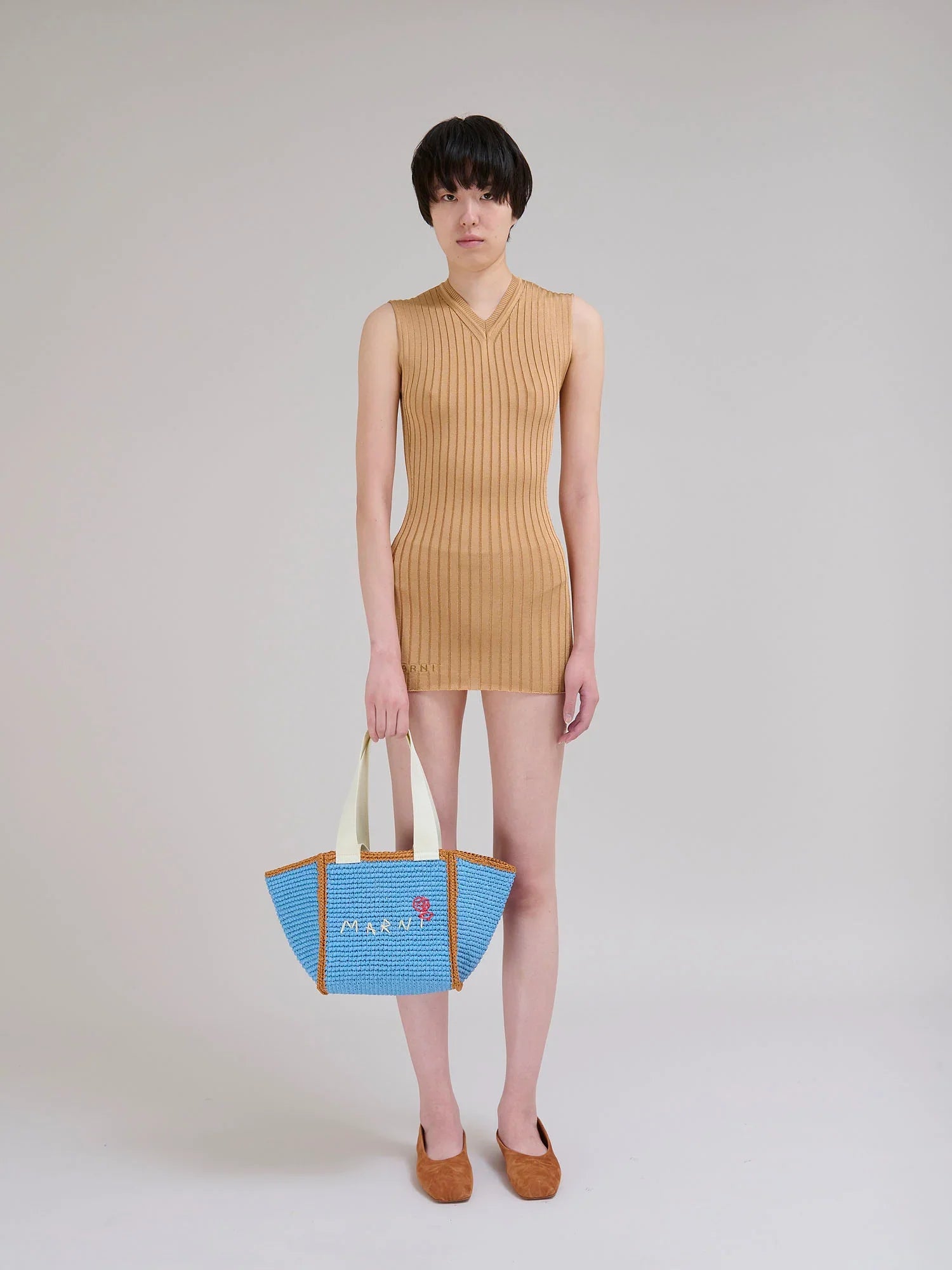 Model in a sleeveless camel ribbed knit mini dress holding a blue and orange Marni tote bag with beige handles