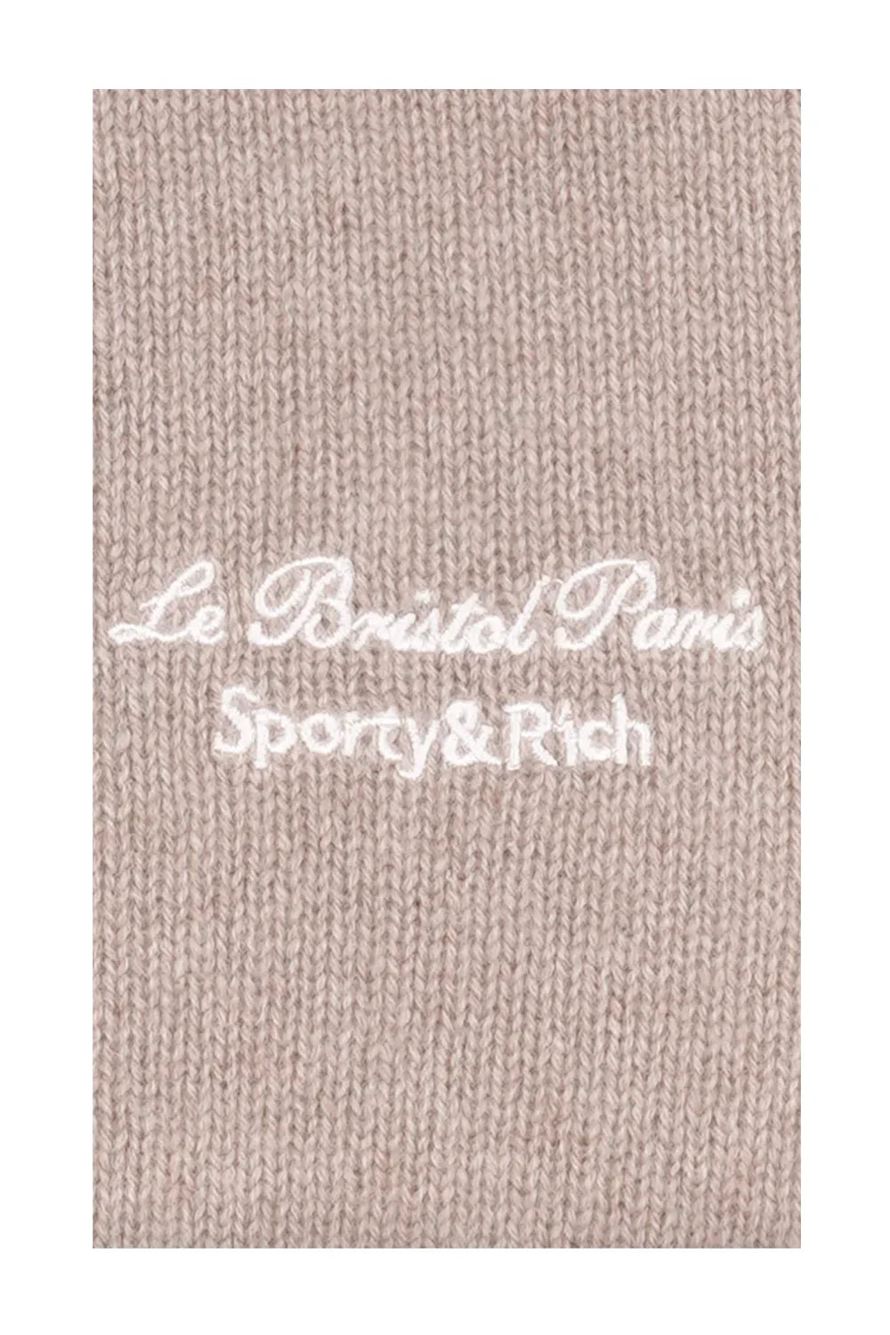 Close-up of beige knitted fabric with embroidered white text Le Bristol Paris Sporty & Rich