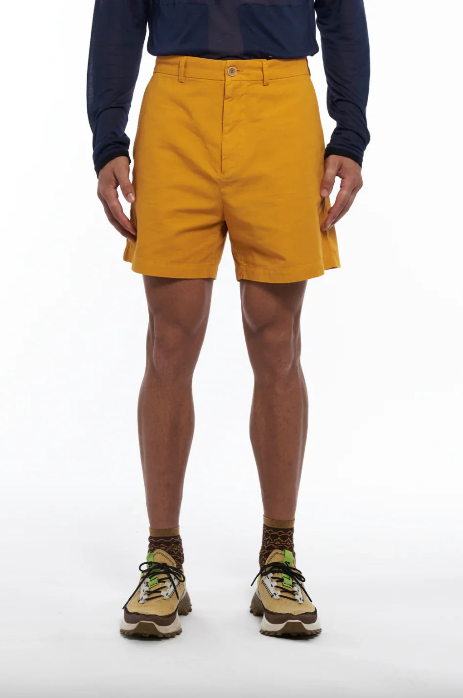 Man wearing mustard yellow shorts, patterned brown socks, and beige hiking shoes against white background
