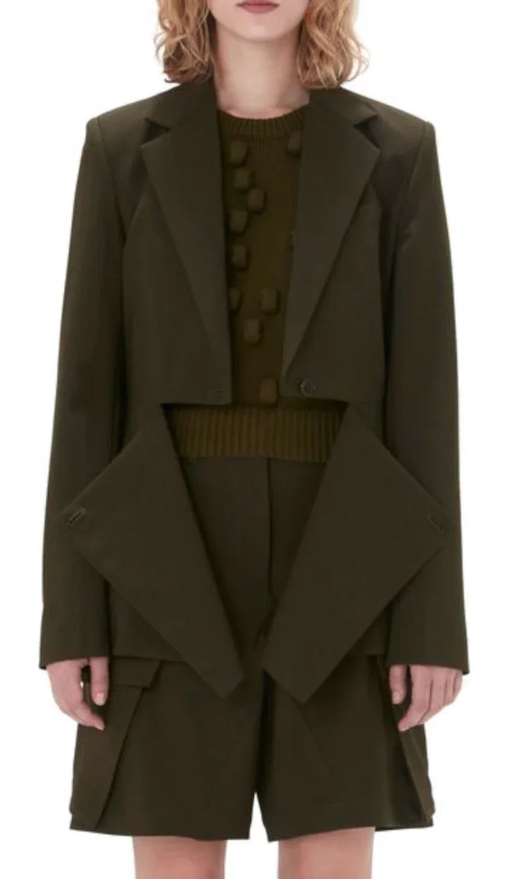 Woman wearing dark olive green blazer with oversized lapels and matching shorts, paired with textured knit sweater