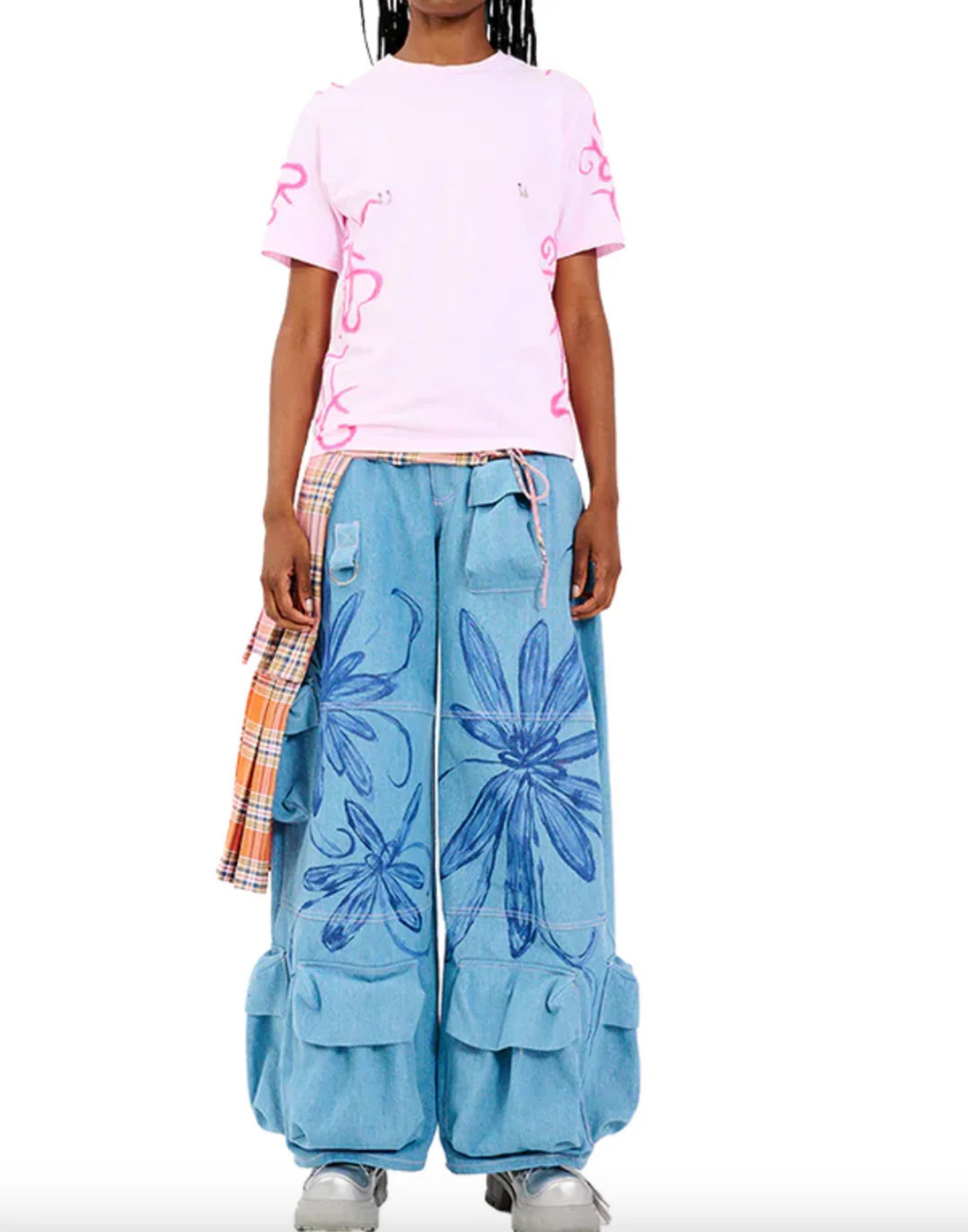 Model wearing pink graphic t-shirt and wide-leg denim pants with large blue floral prints and orange plaid detail