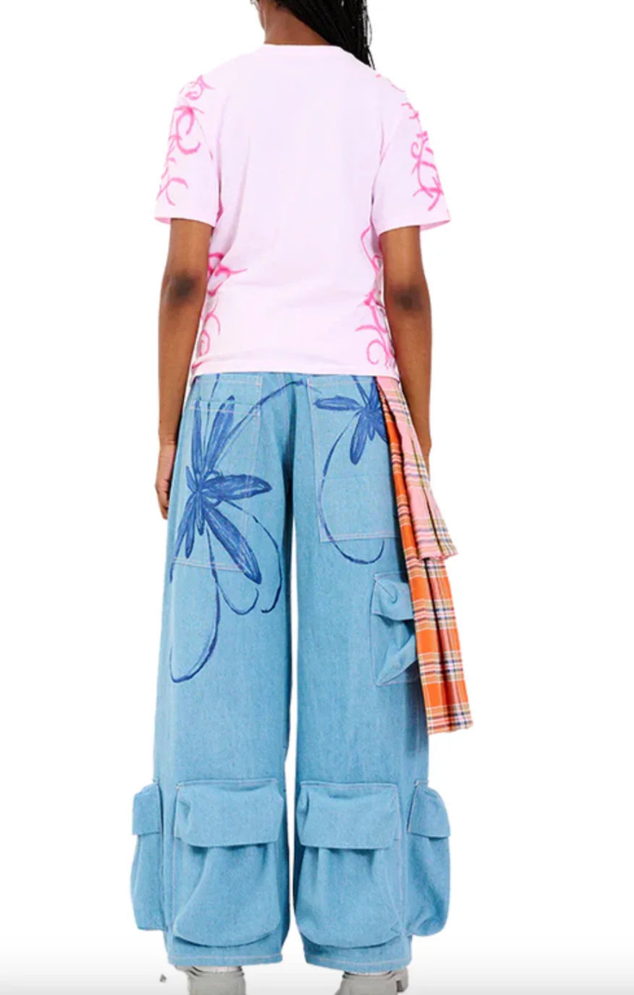 Back view of a person wearing pink graphic t-shirt and light blue wide-leg cargo pants with blue floral prints and attached plaid fabric