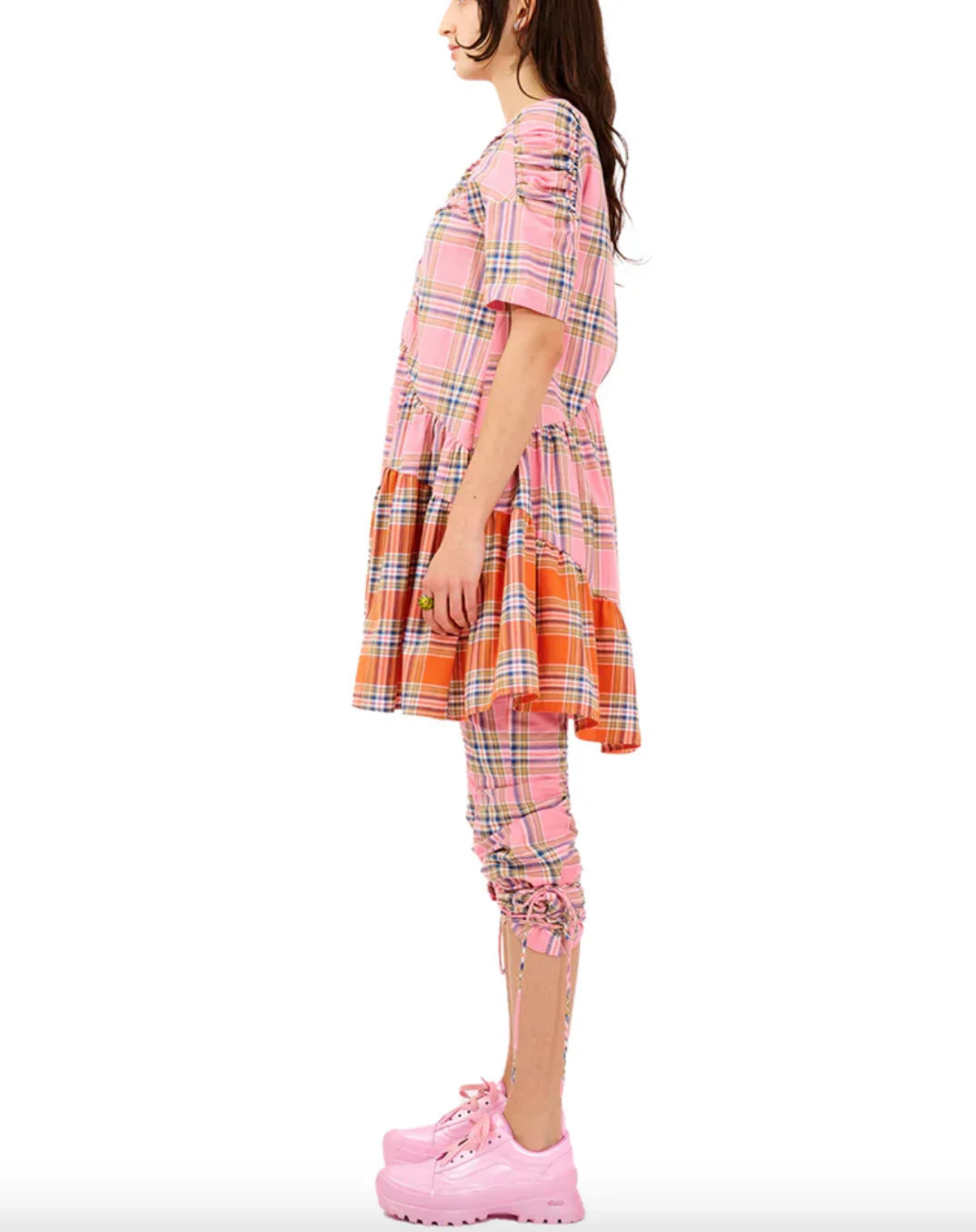 Side view of woman wearing pink and orange plaid dress with ruched leggings and pink platform shoes