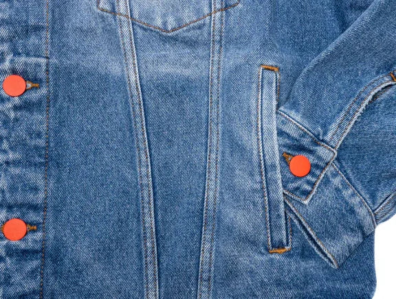 Close-up of blue denim jacket with orange buttons and detailed stitching on pocket and sleeve