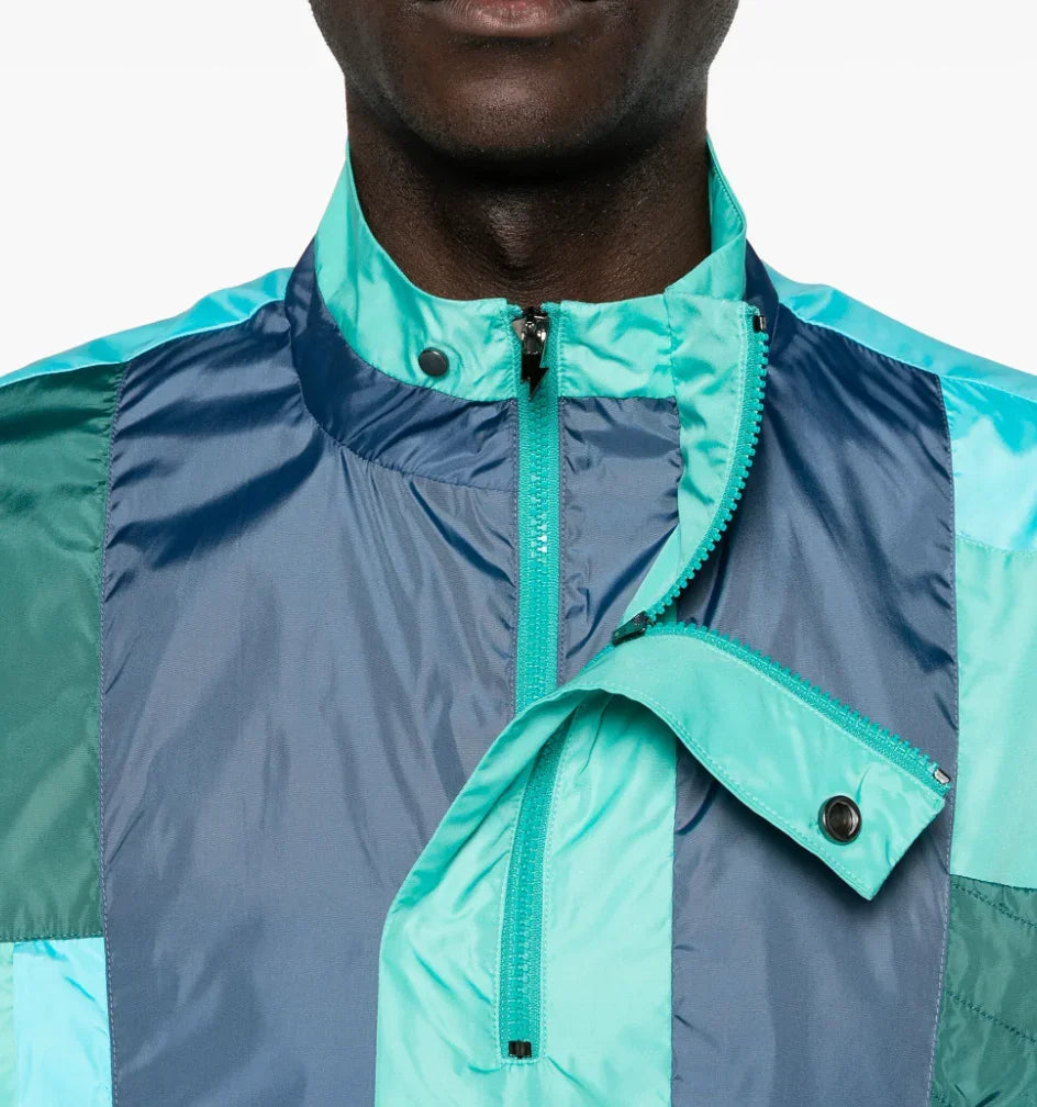 Close-up of man wearing teal and navy colorblock windbreaker jacket with zipper and snap collar