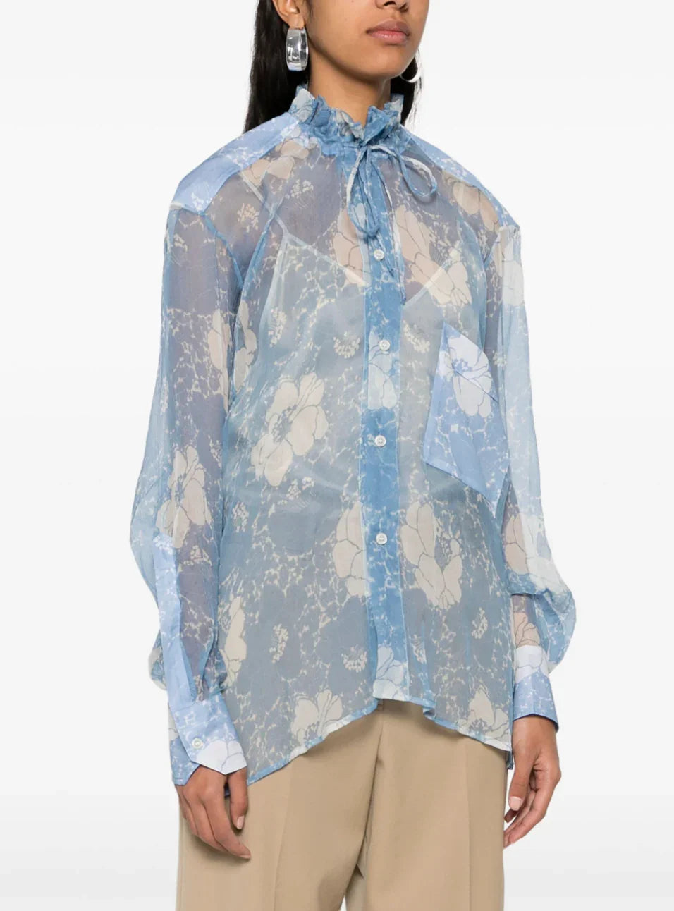 Woman wearing sheer blue floral blouse with ruffled collar and oversized sleeve cuffs