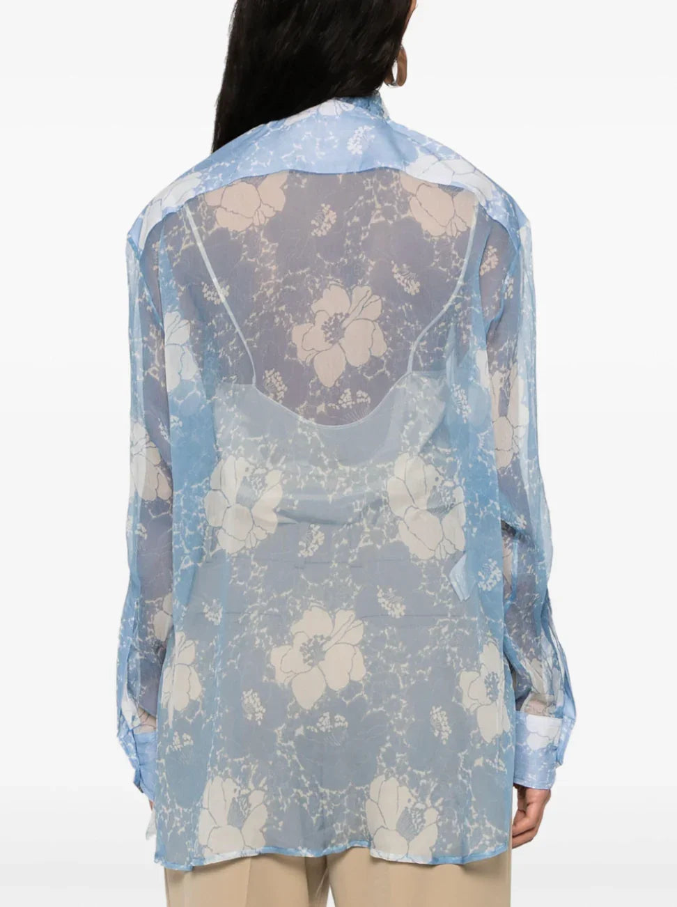 Back view of woman wearing sheer blue floral lace blouse over beige top and pants