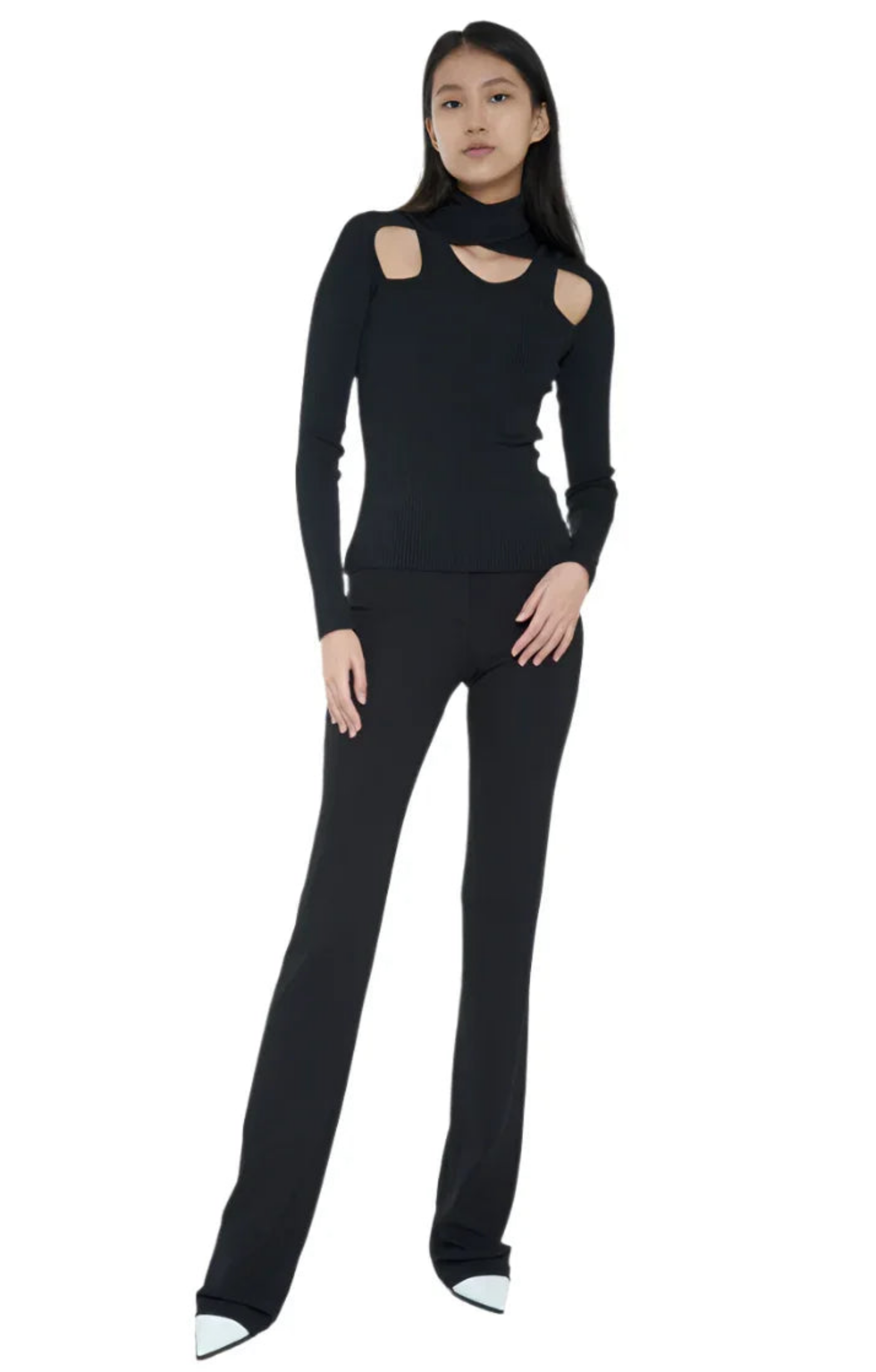 Woman wearing black cutout long sleeve top and black pants with white pointed shoes on white background