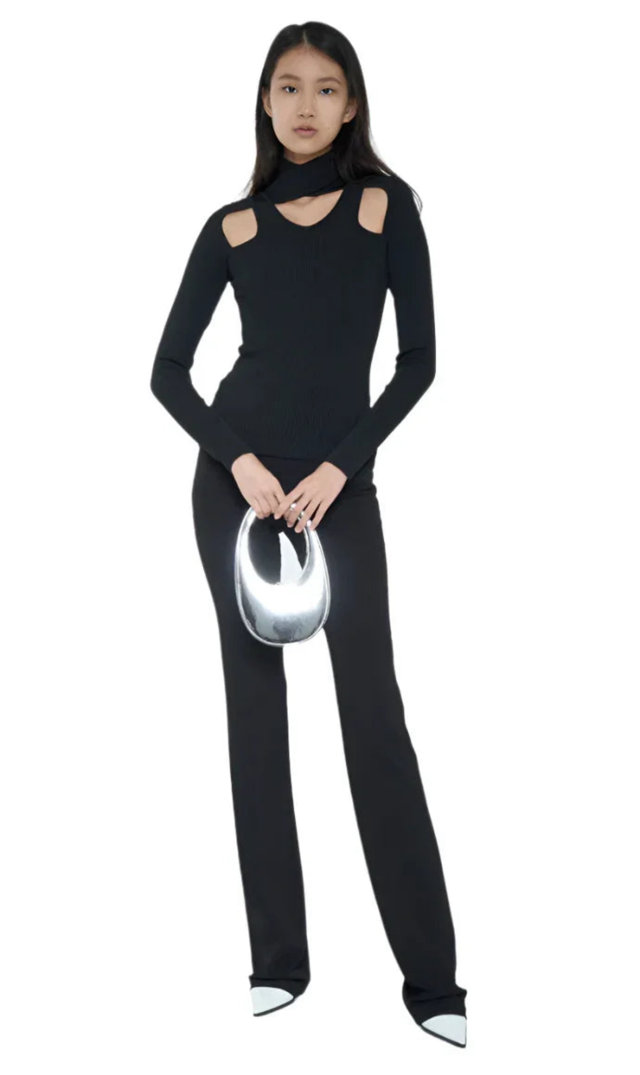 Woman in black cutout long-sleeve top, black pants, white pointed shoes, holding shiny silver handbag