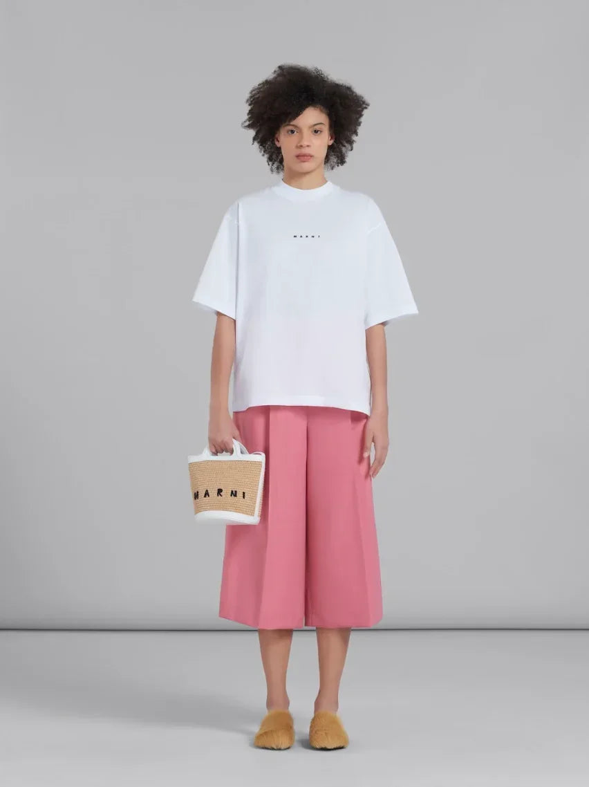 Model wearing white oversized t-shirt, pink wide-leg culottes, fuzzy slippers, holding Marni straw bag