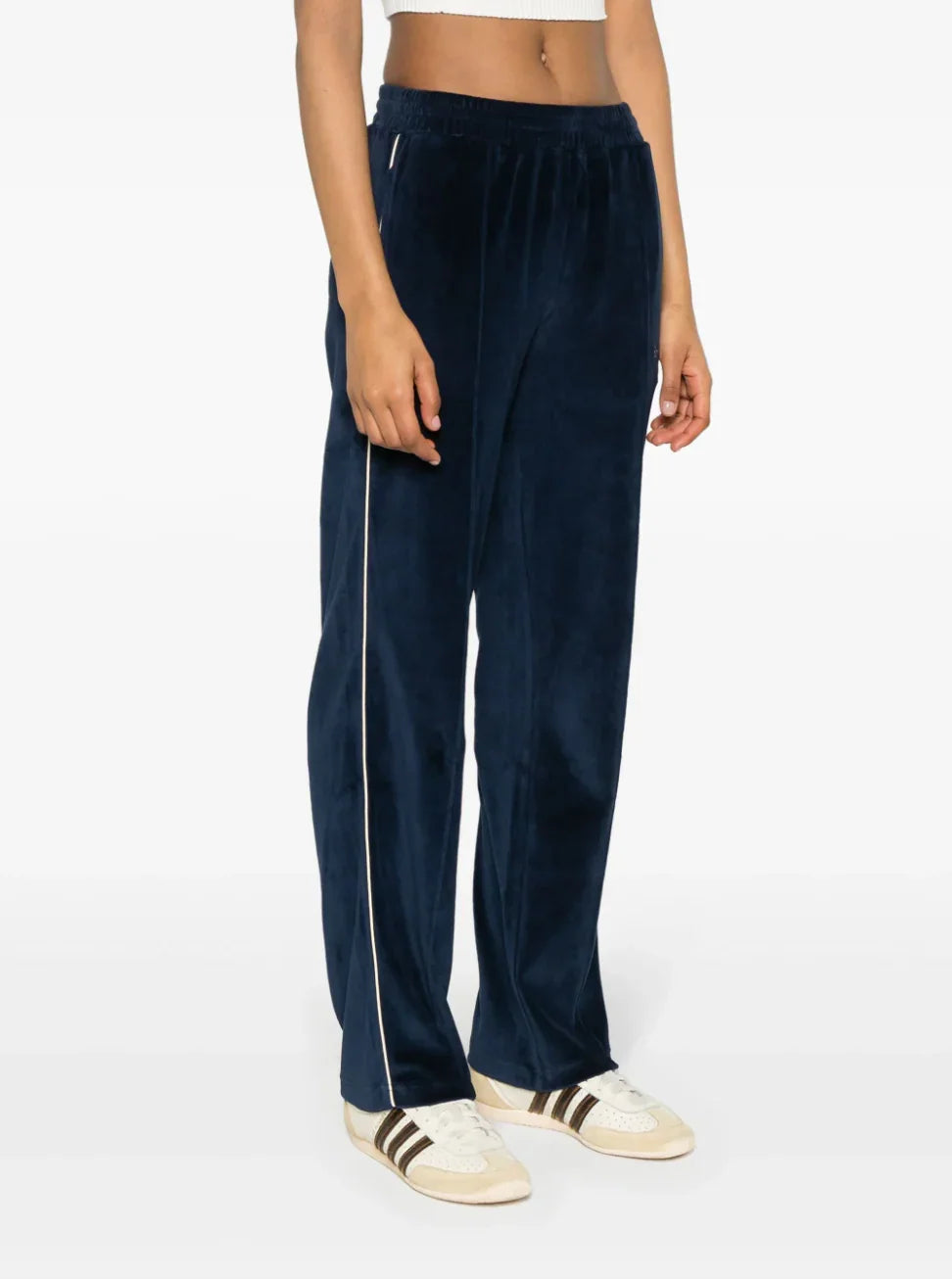 Woman wearing navy blue velour track pants with white side stripe and white sneakers