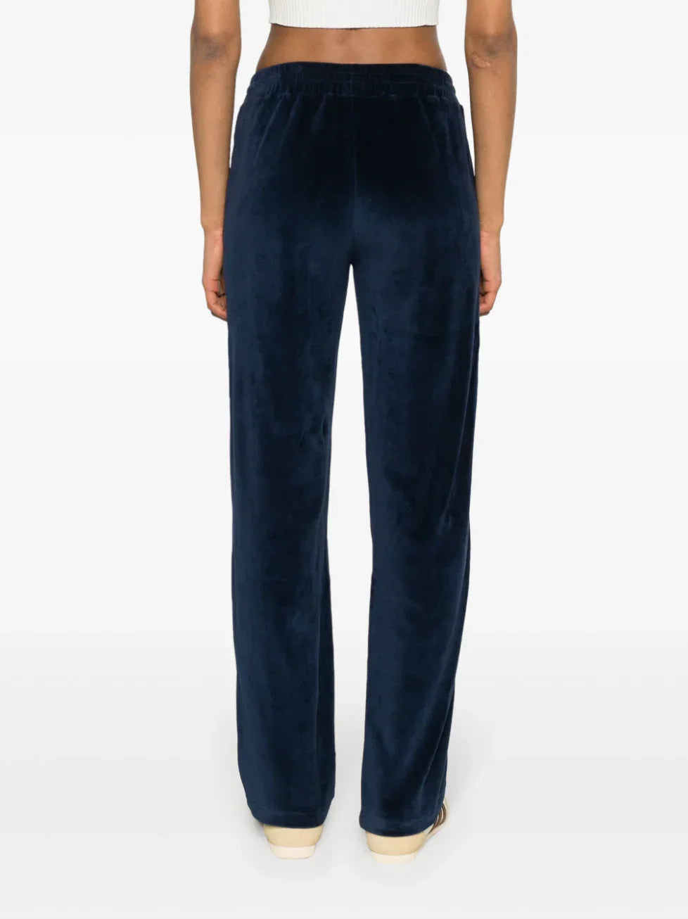 Back view of woman wearing navy blue velour lounge pants with elastic waistband and cream shoes