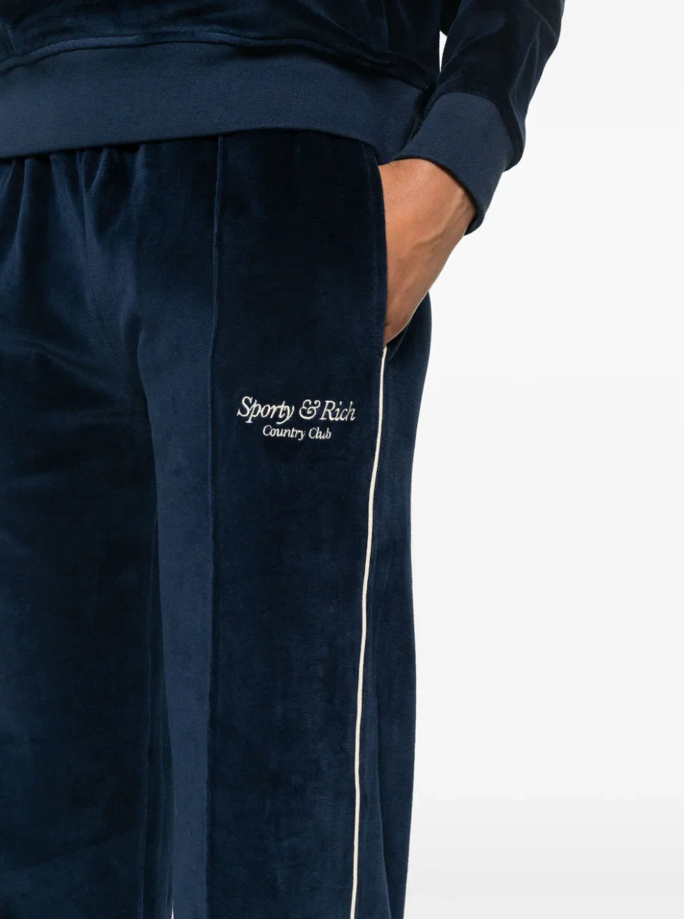 Close-up of navy blue Sporty & Rich velour sweatpants with white piping and embroidered logo on pocket