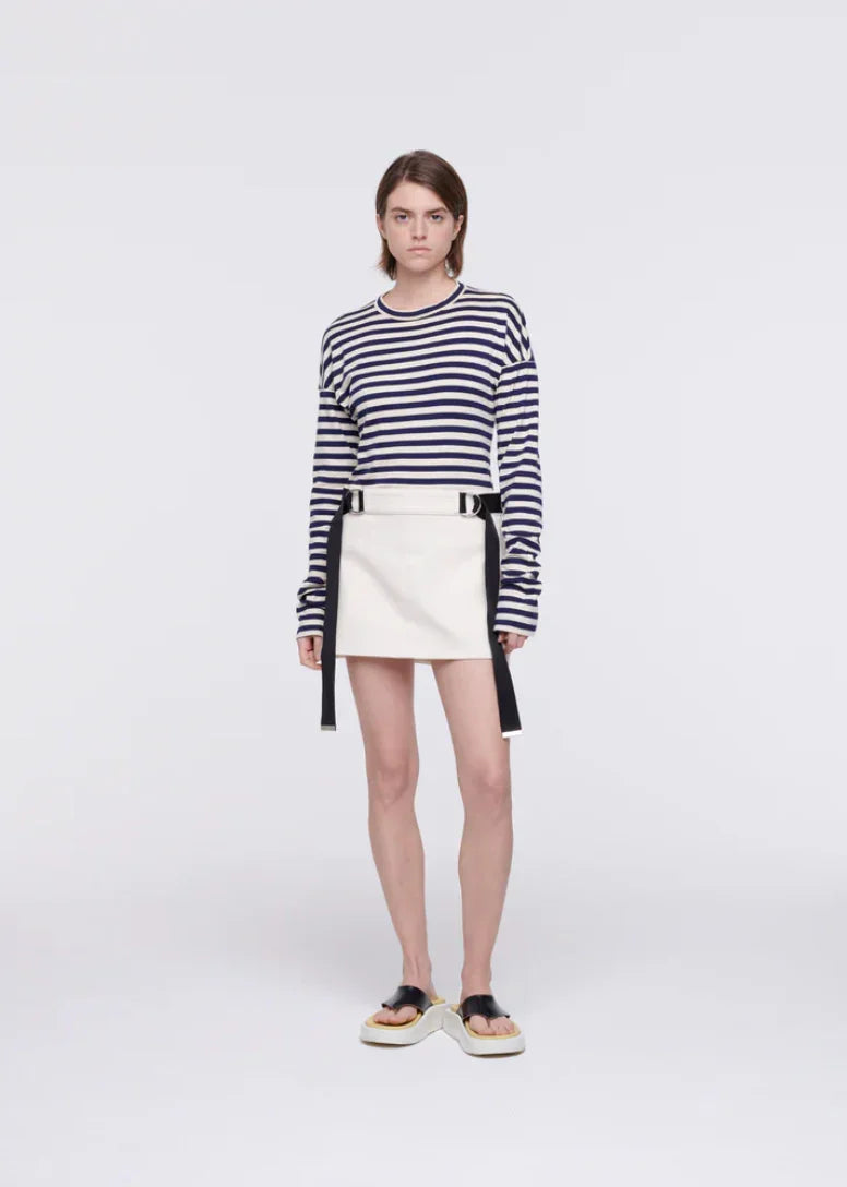 Model wearing navy striped long-sleeve top, white mini skirt with black straps, and platform sandals