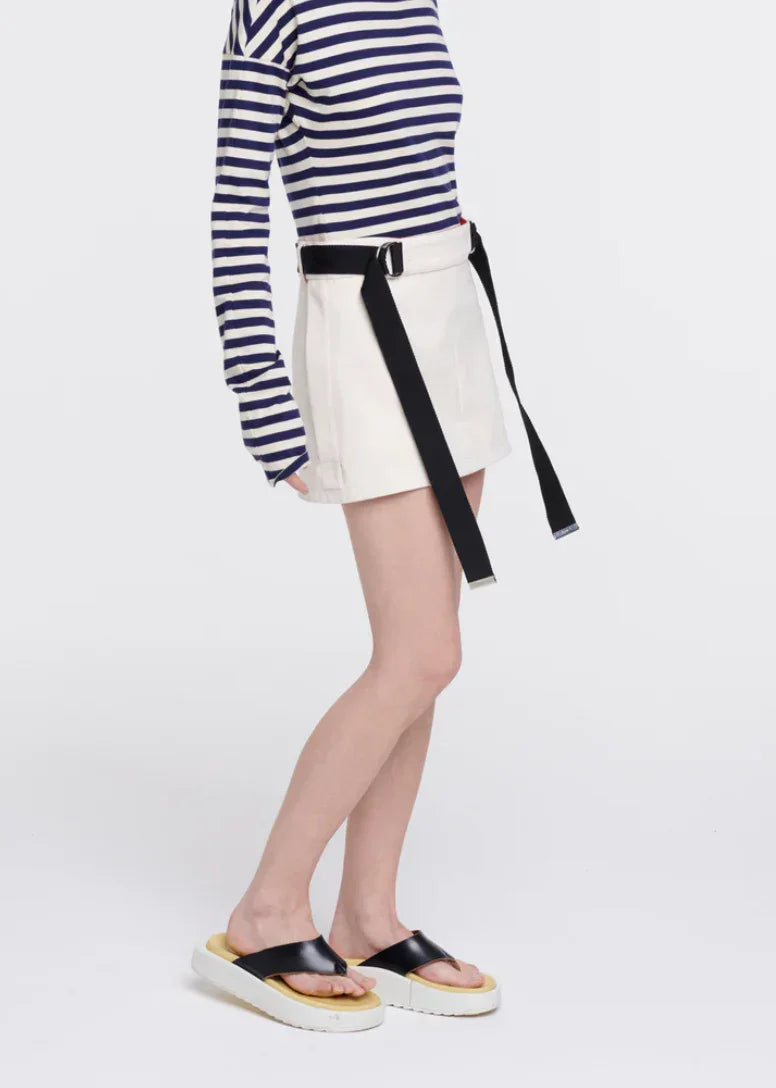 Woman wearing white mini skirt with black belt, navy striped long sleeve top, and black platform sandals