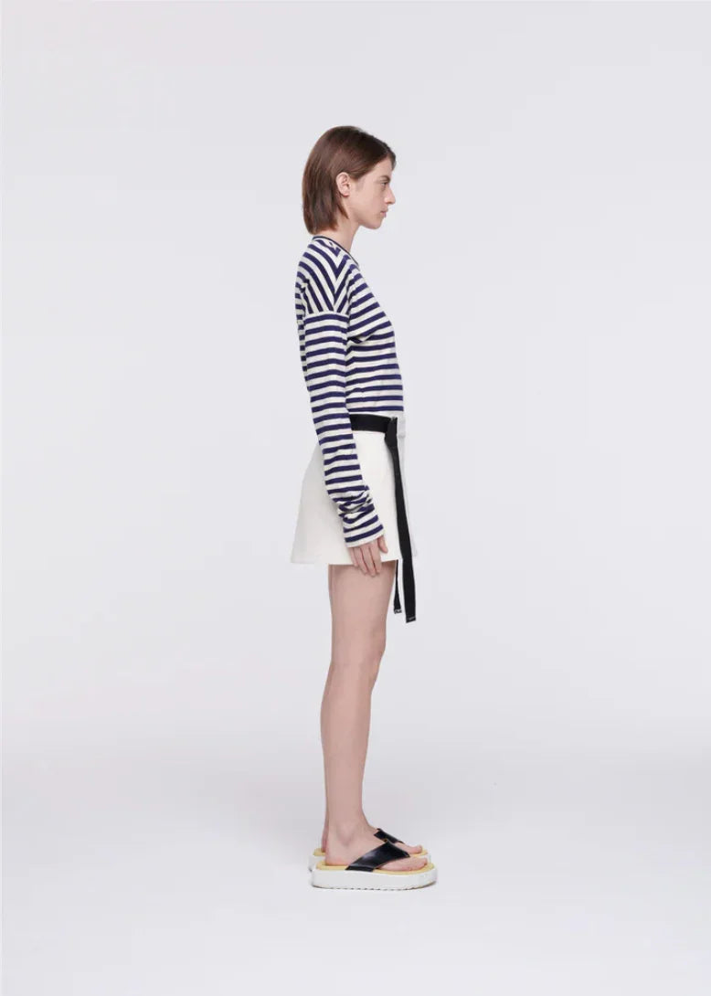 Profile of woman wearing navy striped long-sleeve top, white mini skirt with black belt, and platform sandals