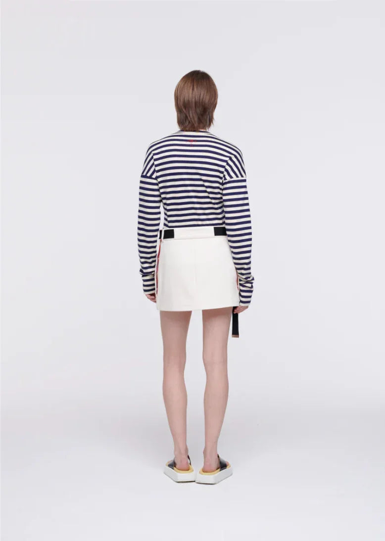 Model wearing navy striped long-sleeve top and white mini skirt with black belt, back view