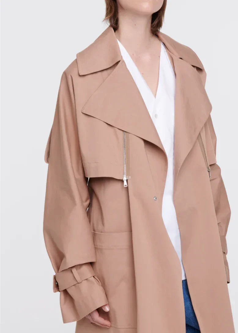 Close-up of woman wearing beige trench coat with wide lapels and zipper detail over white shirt