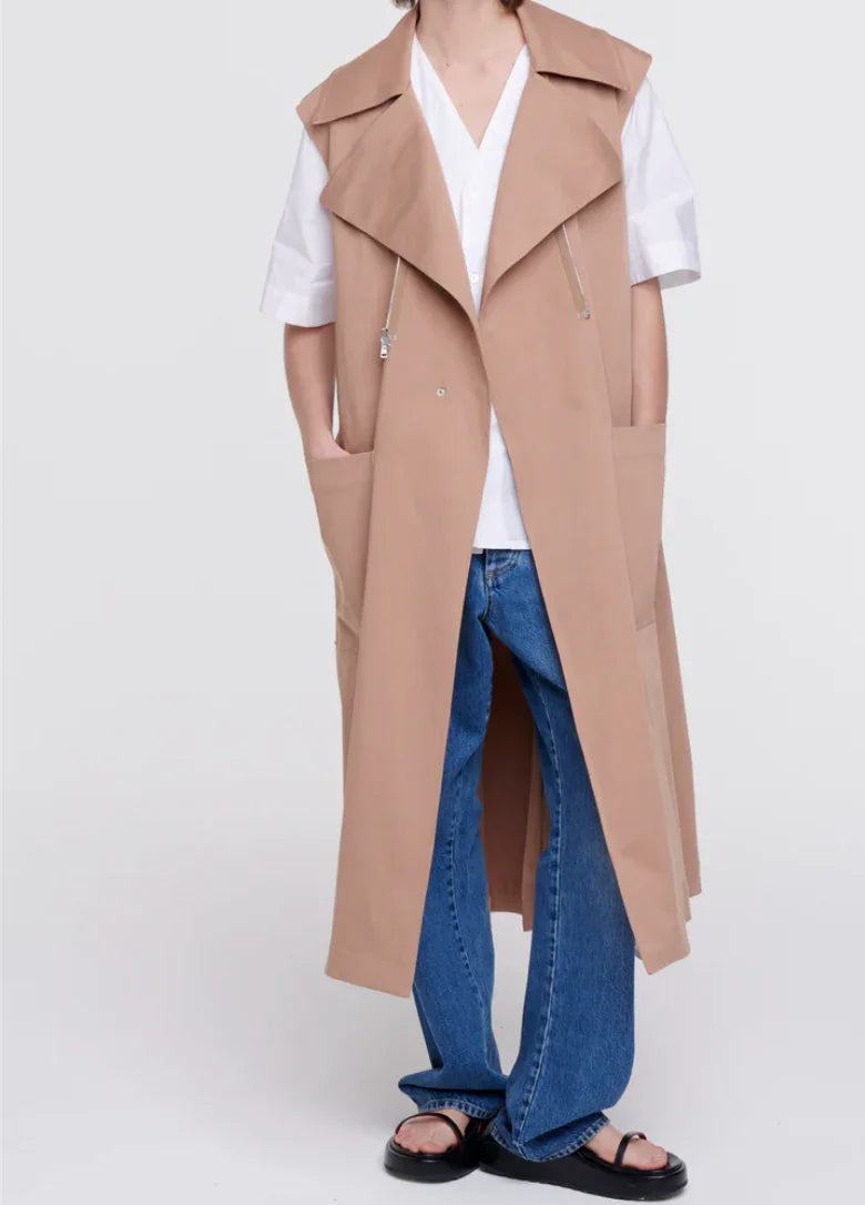 Casual outfit featuring beige sleeveless trench coat, white shirt, blue jeans, and black sandals