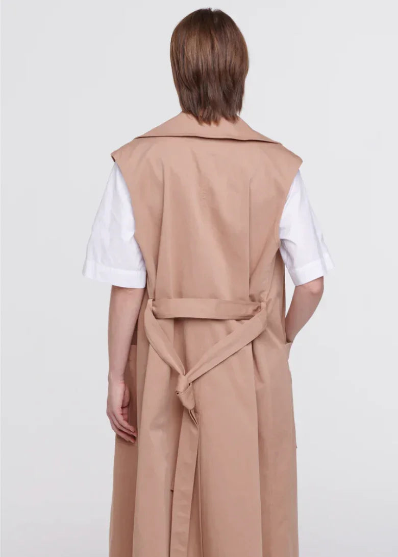 Back view of person wearing beige sleeveless trench coat over white shirt with elbow-length sleeves