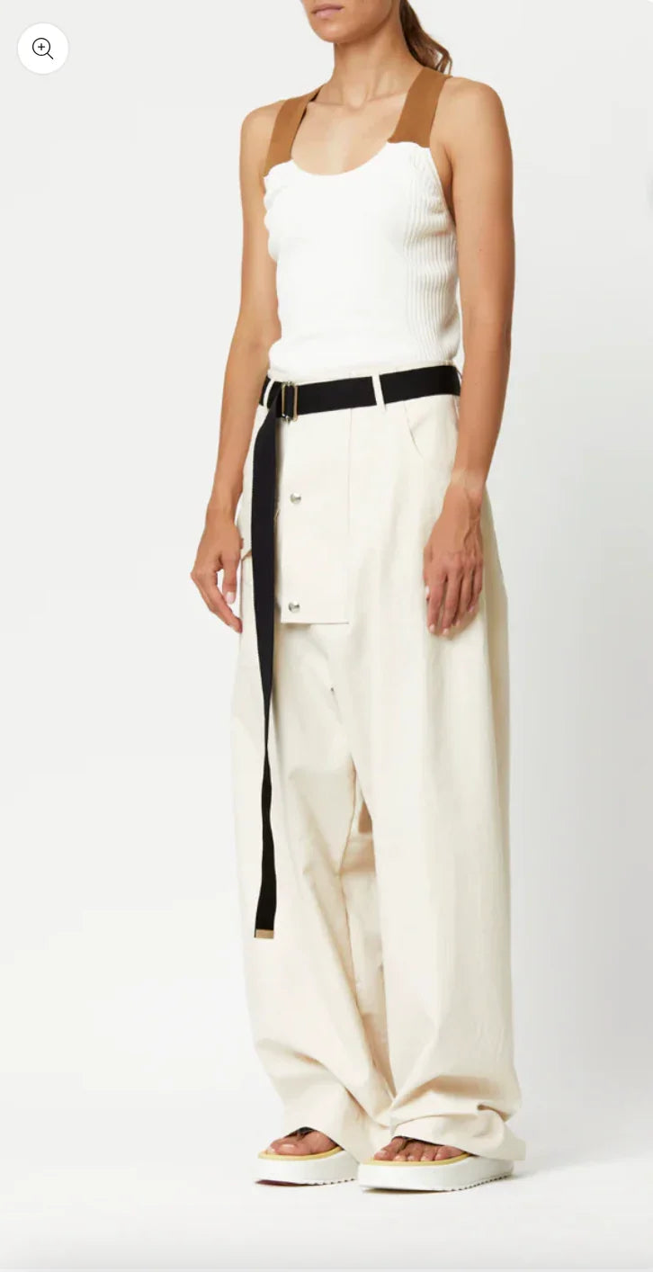 Woman wearing white sleeveless ribbed top with brown straps and wide-leg cream pants with black belt