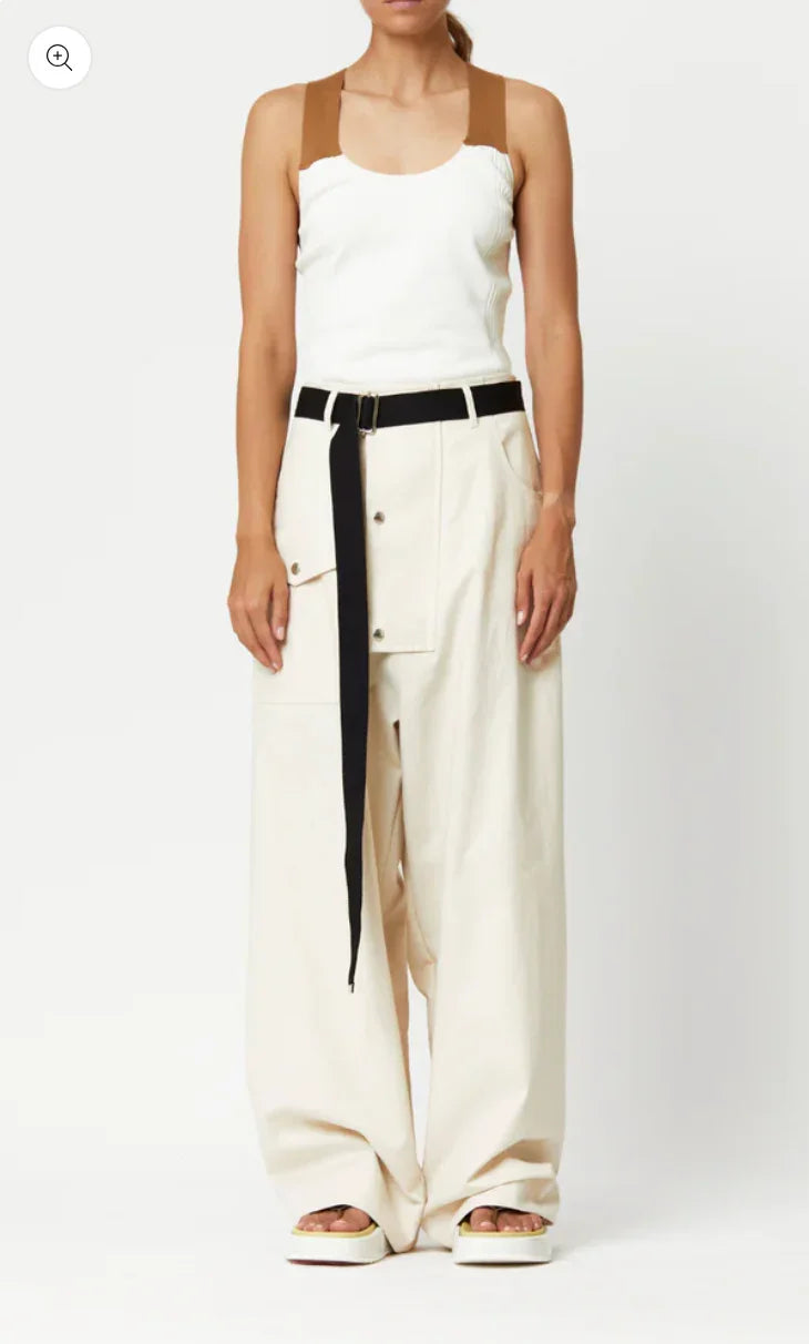 Woman wearing white wide-leg pants with black belt and white sleeveless top with brown straps