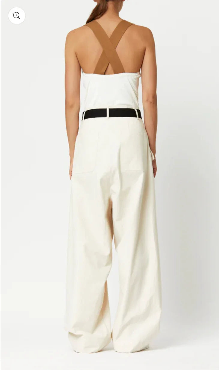Back view of woman wearing white high-waisted wide-leg pants with black belt and white camisole with brown crossed straps