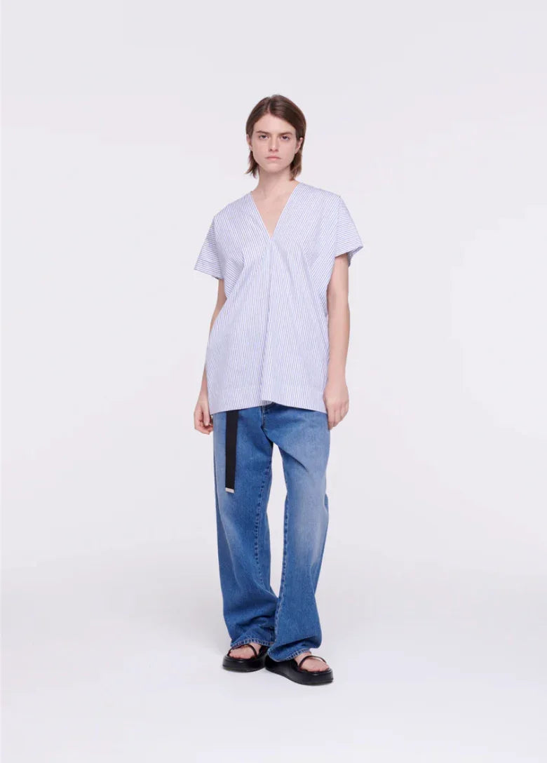 Model wearing loose blue jeans with black belt and striped short-sleeve V-neck top on white background