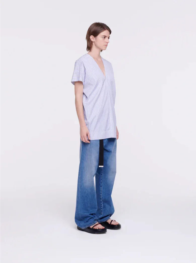Woman wearing blue striped v-neck oversized top and wide-leg denim jeans with sandals on white background