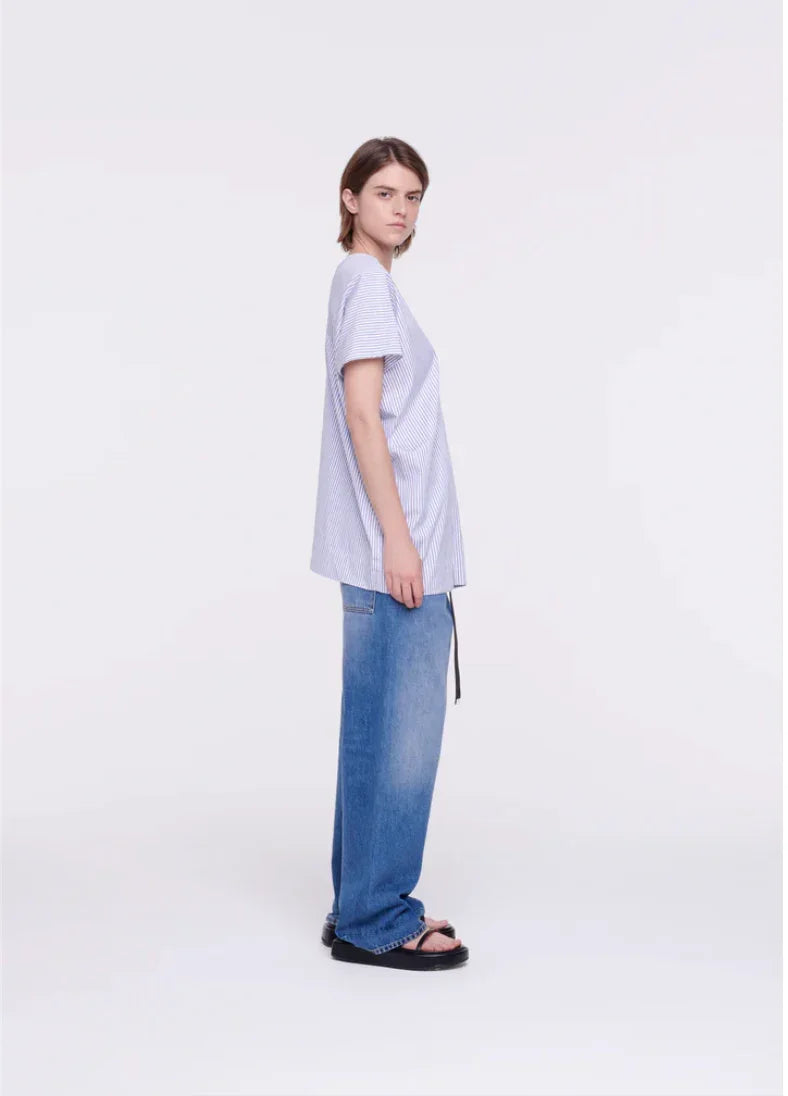 Young woman in striped short-sleeve shirt, baggy blue jeans, and black sandals posing in studio