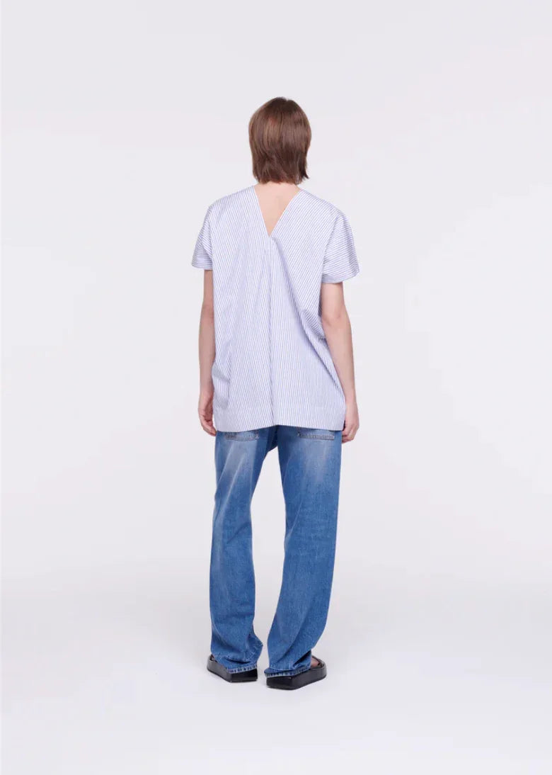 Person wearing loose blue striped short-sleeve top with V-back and relaxed blue jeans on white background