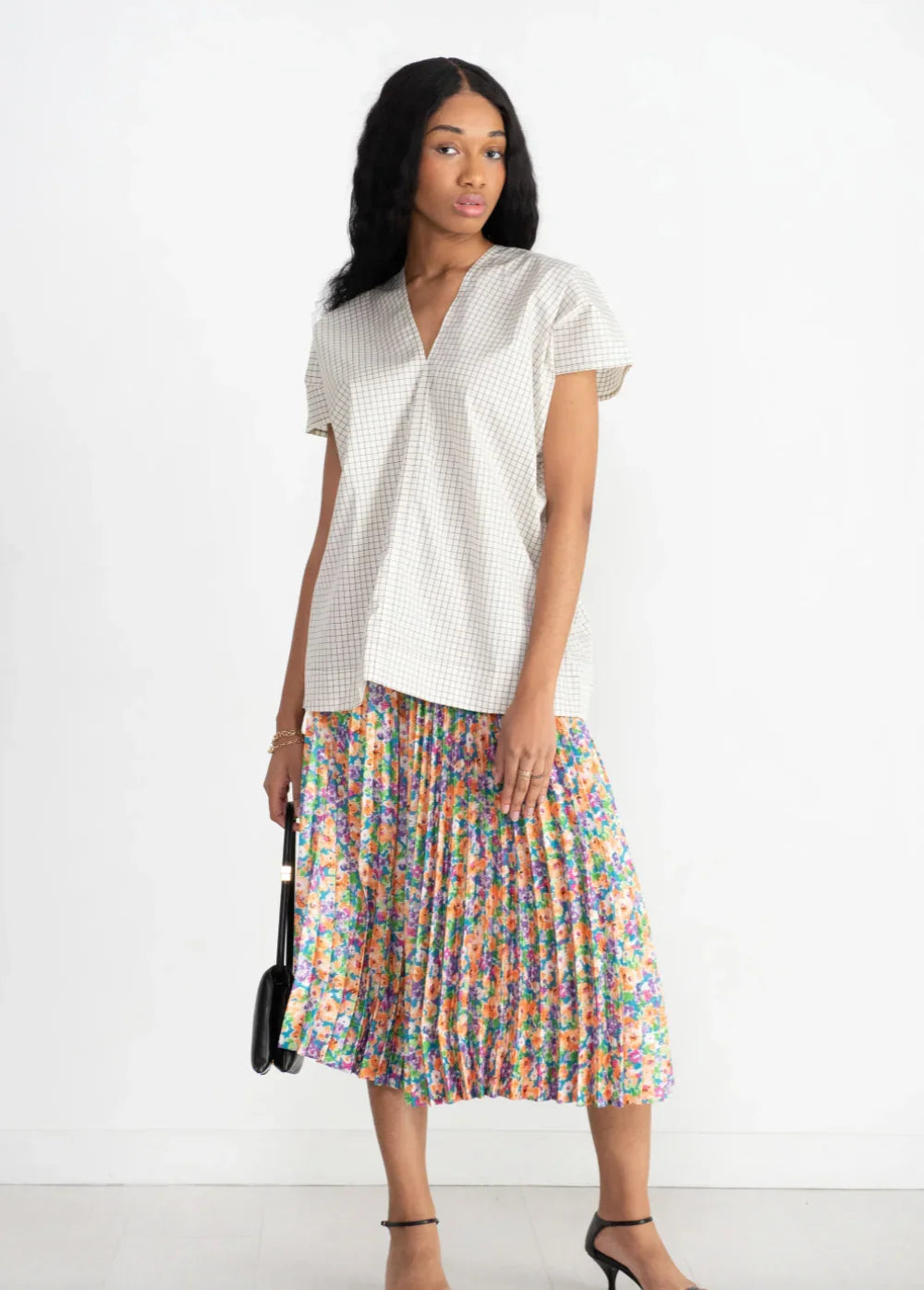 Woman in checked light blouse and colorful floral pleated midi skirt in studio fashion shoot
