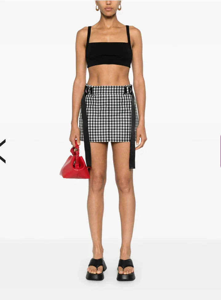Model wearing black crop top, black and white checkered mini skirt with black straps, black sandals, red handbag