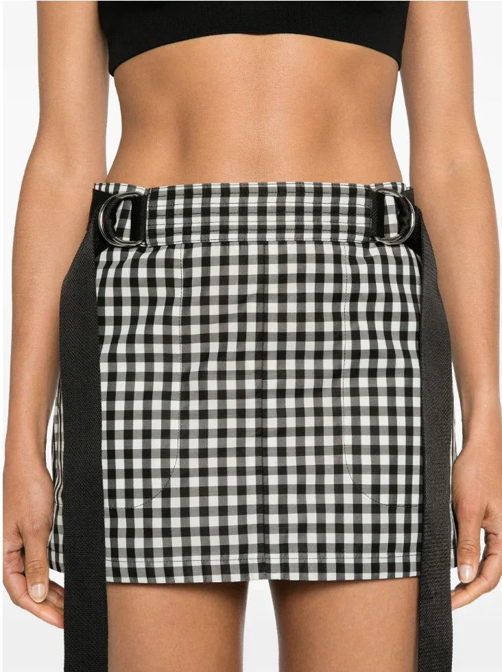 Close-up of a black and white checkered mini skirt with black belt straps and silver rings on a woman