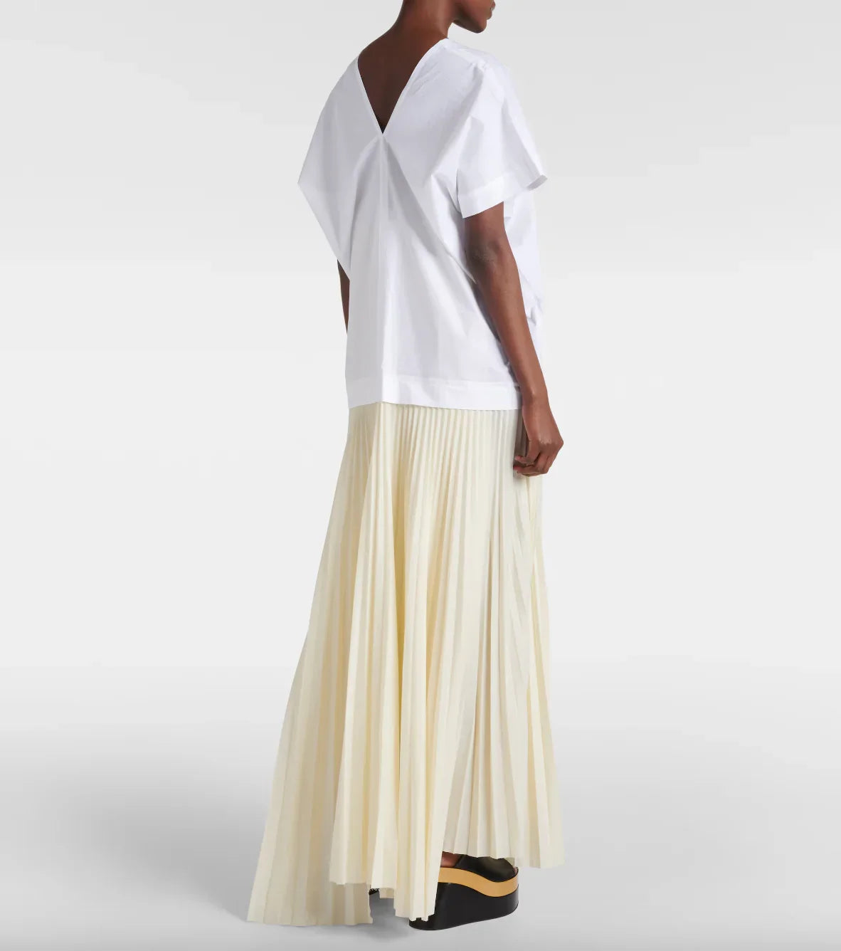 Woman wearing white V-back top and cream pleated maxi skirt with black platform shoes