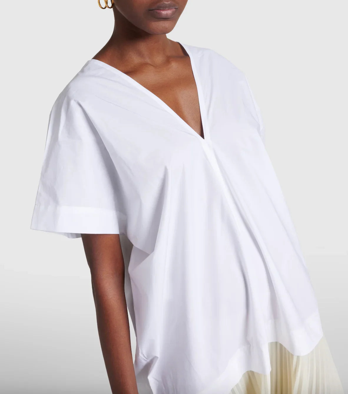 Close-up of a woman wearing a loose white V-neck short sleeve blouse with pleated light skirt