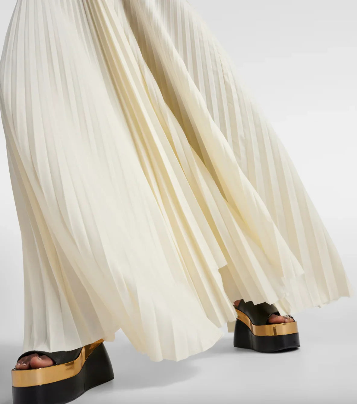 Close-up of white pleated maxi skirt paired with black and gold platform sandals