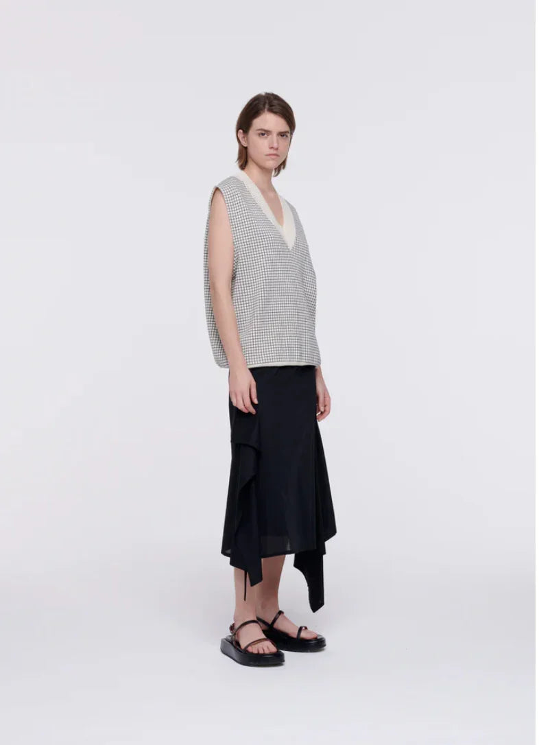 Model wearing sleeveless checkered vest with deep V-neck and black asymmetrical midi skirt with platform sandals