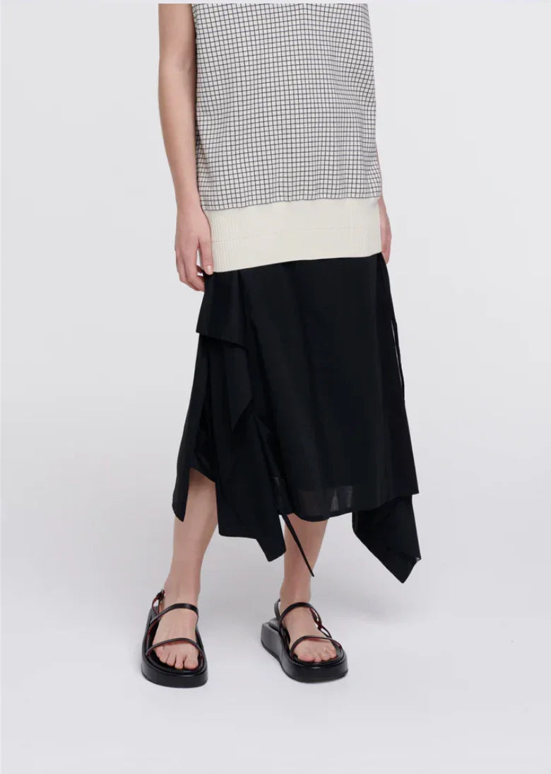 Woman wearing black asymmetrical midi skirt, black strappy sandals, and sleeveless checkered top