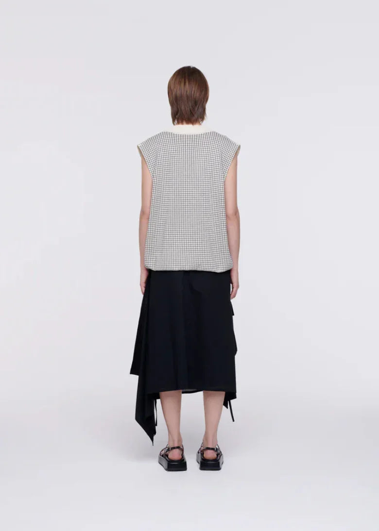Back view of woman wearing sleeveless checkered top, asymmetrical black skirt, and platform sandals
