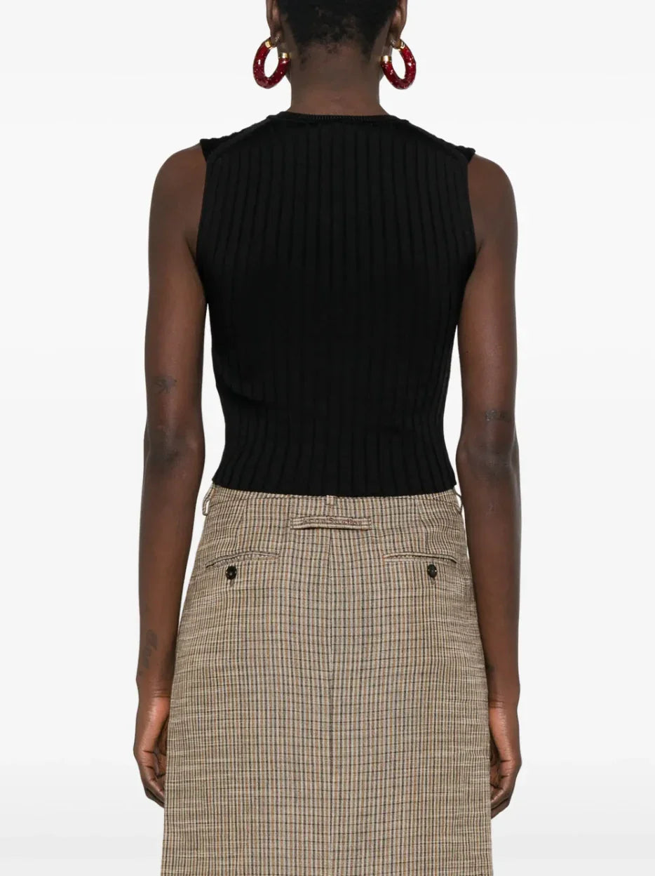 Back view of woman wearing black ribbed sleeveless top and beige plaid skirt with pockets