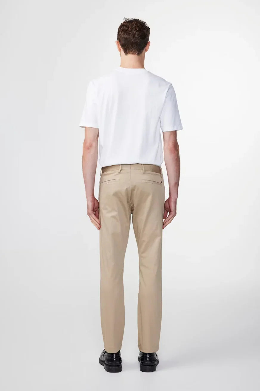 Man wearing white t-shirt and beige chinos with black shoes standing against white background