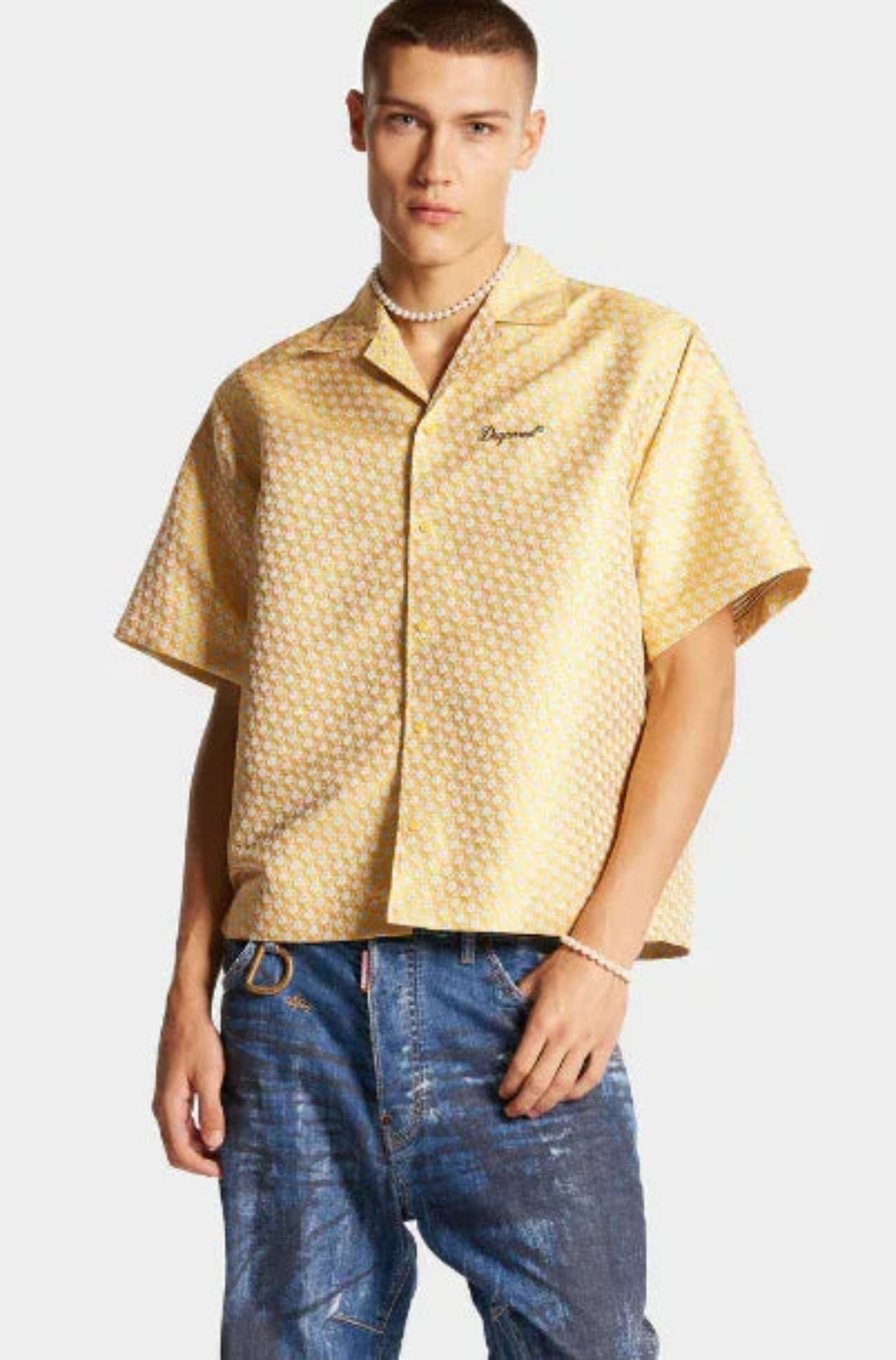 Man wearing yellow patterned short-sleeve shirt and blue denim jeans with pearl necklace and bracelet