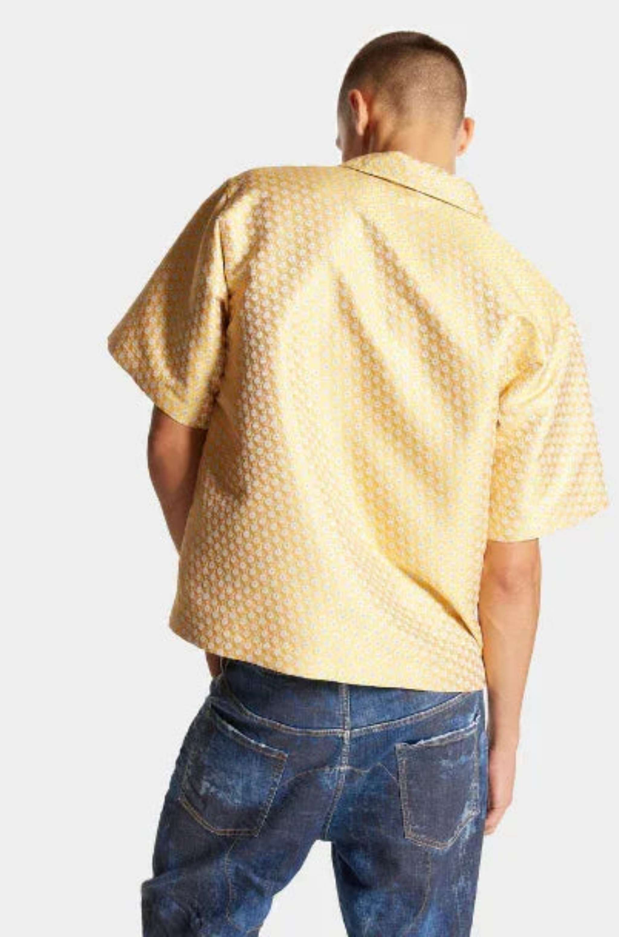 Rear view of man wearing yellow patterned short-sleeve shirt and blue distressed jeans